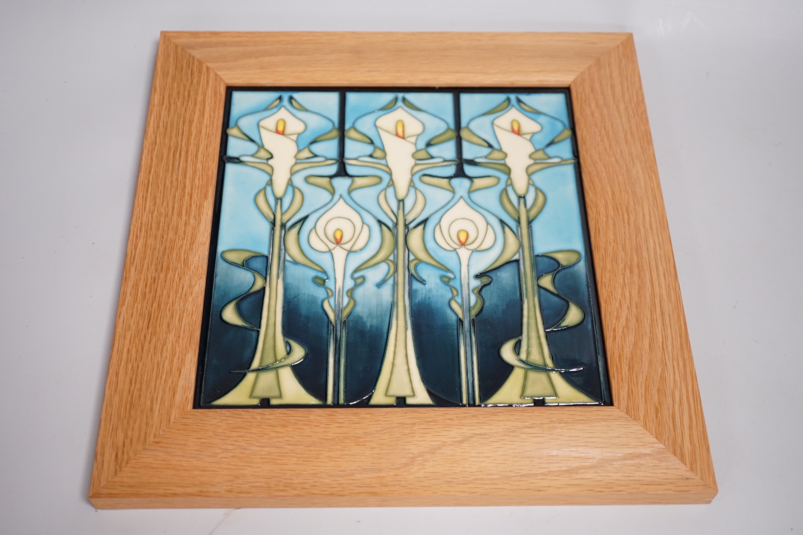 Two framed Moorcroft tiles, one with stylised lilies, the smaller tile with cyclamen, larger tile 21.5cm x 21.5cm
